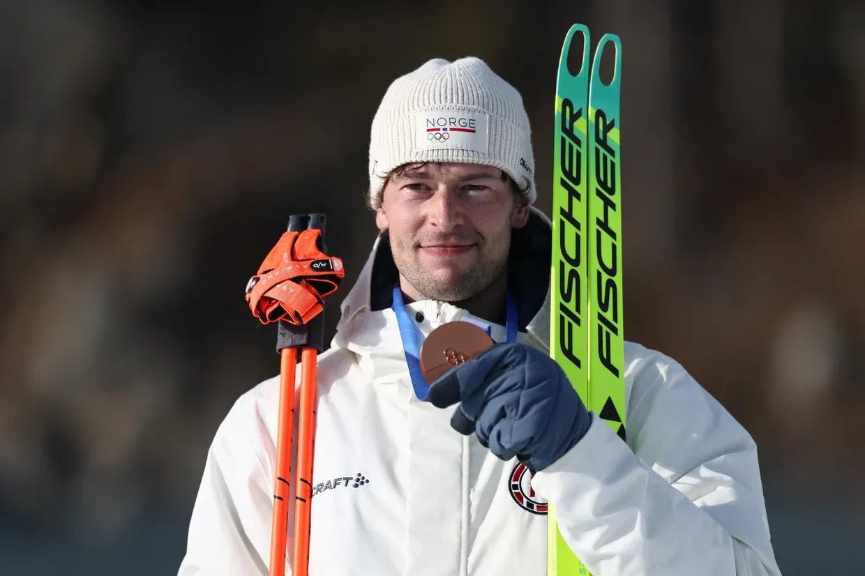 The cheating Norwegian biathlete holding his skis, his poles, and a bronze medal.